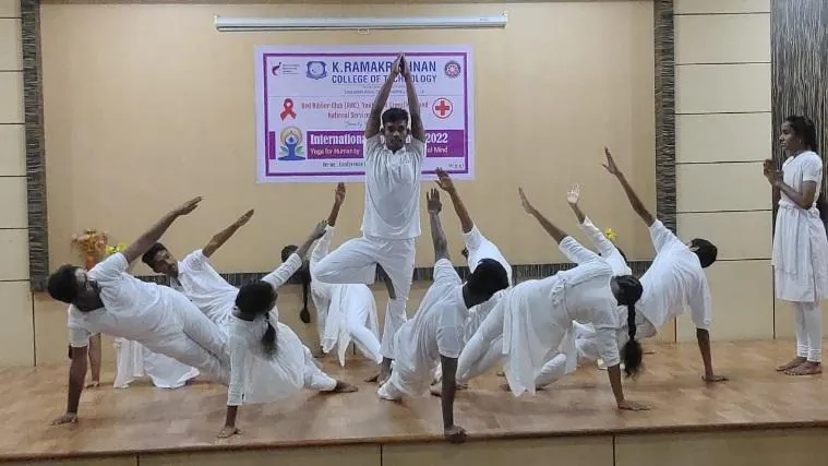 Students in white performing a group asana on stage